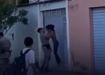 Policial tira mulher do chão pelo pescoço e a joga contra portão