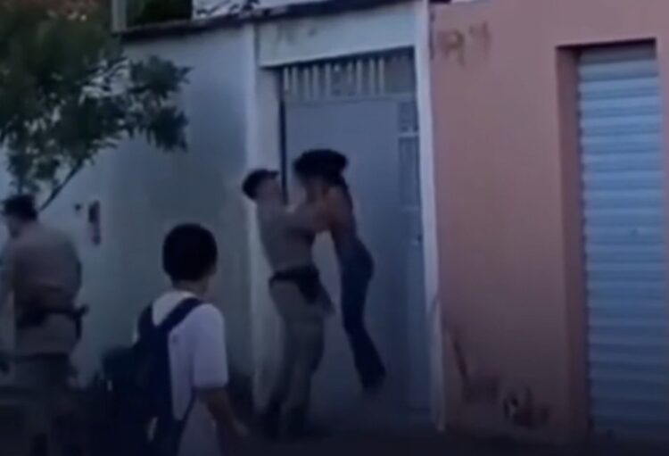Policial tira mulher do chão pelo pescoço e a joga contra portão